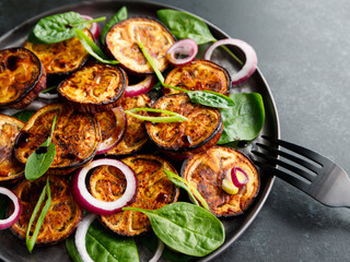 Salad with grilled eggplant, spinach, purple onion and sauce on a dark table.