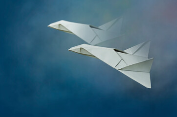 Two white paper jets fly in the clouds