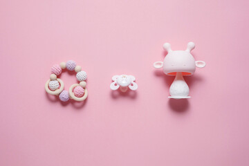 Baby accessories concept: teether, caterpillar toy and baby pacifier, over pink background with copy space, top view, flat lay.