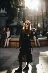 Fototapeta premium a young girl in rocker black clothes and long hair walks at sunset in the city