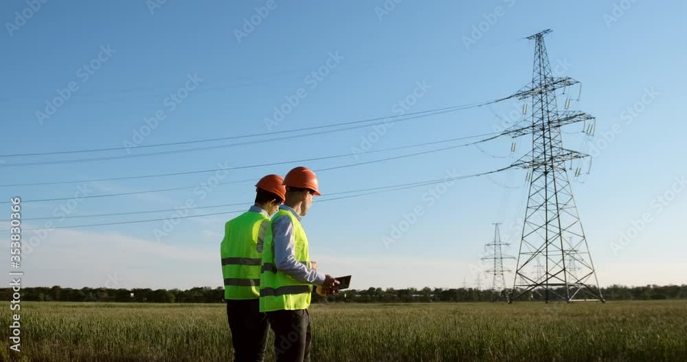 Wall mural two engineers in a special form discuss the power line modernization plan with a high-voltage line i