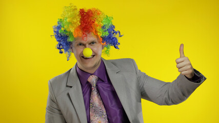 Clown businessman entrepreneur boss in wig show thumb up. Yellow background