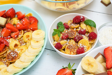 tiny pancake cereal bowl with fresh strawberries banana chocolate, coconut shavings and honey in small plates. the view from the top . the trend of self-isolation