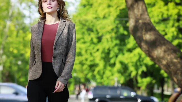 Smiling woman in stylish look walking down street in park in daytime. Urban, street, lifestyle concept