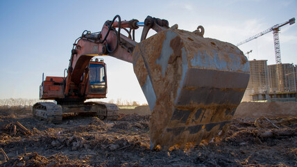 Large excavator working at construction site. Backhoe during earthworks on sand open-pit. Digging ground for the foundation and for laying sewer pipes district heating. Earth-moving heavy equipment