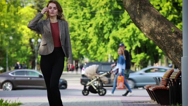 Smiling woman in stylish look walking down street in park in daytime. Urban, street, lifestyle concept