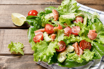 Salmon salad with avocado, green leaves, tomatoes on wooden background