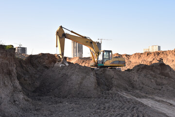 Obraz premium Excavator working at construction site on earthworks. Backhoe digging building foundatio. Construction machinery for excavating, loading, lifting and hauling of cargo