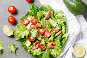 Salmon salad with avocado, green leaves, tomatoes on gray background