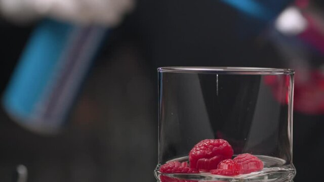 Cooking Raspberry Sambuca. Close up barmans hand sets fire to sambuca in snifter and pours it into a glass with raspberries. Then he covers the glass. Steam rises from a hot drink. Glass slowly moving