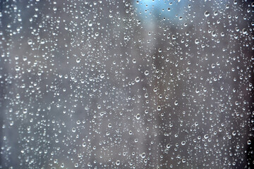 Fototapeta na wymiar Raindrops on the transparent window pane. Rainy weather outside the window. Abstract background with transparent drops of rain to wet, gray, and opaque glass texture for your design.