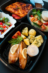 Delivery service food in plastic lunch boxes on a black background. Low key, healthy food, colorful flat lay. Food concept.