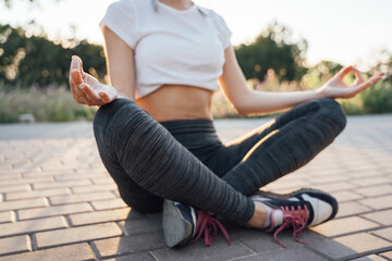 A girl at sunset sits in a lotus pose with headphones in her ears close-up focus on her hand