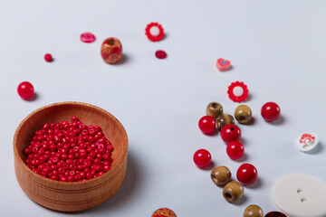 Close up of wooden bowl of red beads and buttons for sewing and embroidery. Set of materials for handcraft, making of bijouterie and accessories. Wooden background, copy space.
