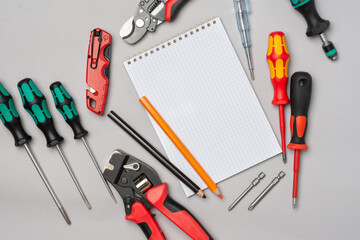 Open the Notepad and tools of an electrician or Builder on the gray table. Concept of drawing up an estimate or list of construction materials. Screwdrivers, crimping, construction knife on the table