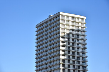 Facade of a new modern high-rise residential building. Skyscraper on blue sky background.  Tall house renovation project, government programs. Minimalistic multi storied home. Urban architecture