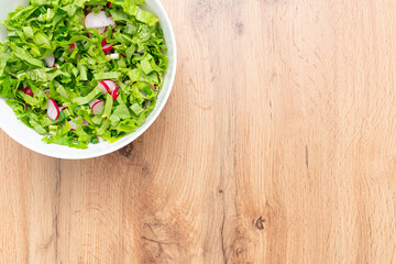 Vitamin spring salad. Salad radishes, lettuce in bowl on wooden table