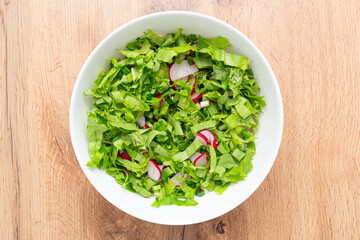 Vitamin spring salad. Salad radishes, lettuce in bowl on wooden table
