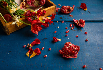 Faded tulips, pomegranate with seeds on dark blue wooden background