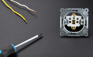 Electrical Work & Repair Costs.A disassembled outlet lies next to a screwdriver on a black background.