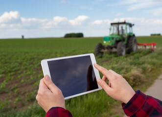 Farmer working on tablet in front of tractor in field