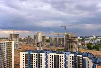 Fototapeta premium Aerial view on the large construction site with tower cranes and builders in action. Multi-storey residential building is being constructed use of crane. Pour of concrete in formwork