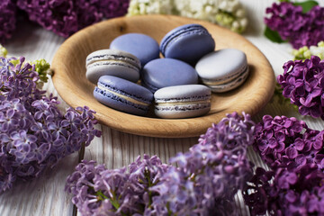
Macaroons in a wooden plate with lilac on a wooden background