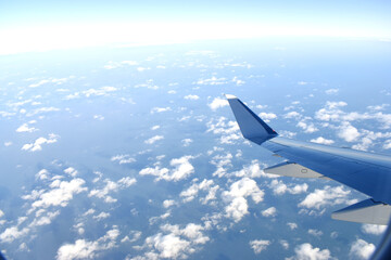 Airplane wing flying above clouds in blue sky, view from airplane window