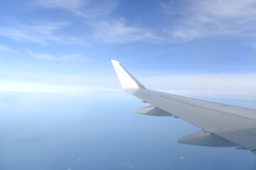 Fototapeta na wymiar Airplane wing flying above clouds in blue sky, view from airplane window