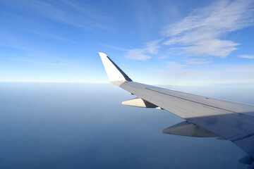 Fototapeta na wymiar White wing of airplane fiying above clouds with horizon blue sky
