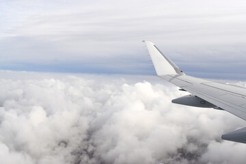 Fototapeta na wymiar Airplane wing view from window, flying above white clouds on the sky