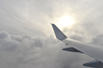 Fototapeta na wymiar Airplane wing fying above white clouds obscure light from the sun