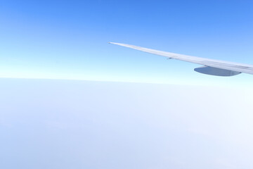 White wing of airplane fiying above clouds with horizon blue sky