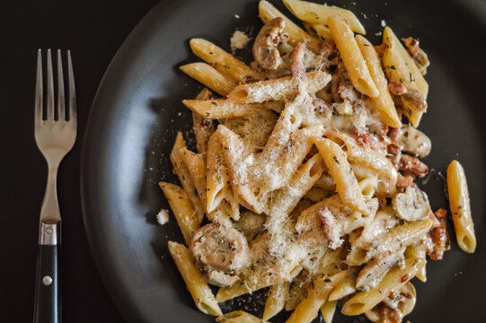 penne pasta and boscaiola topping sauce in a dish with fork closeup - top view