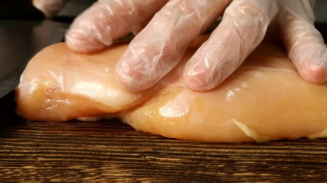 Chef cuts along piece of chicken breast, opens it, beats it with wooden tenderizer and sprinkles salt and pepper on top. Close-up.