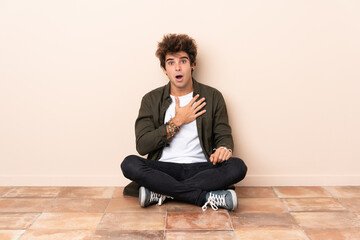 Young caucasian man sitting on the floor surprised and shocked while looking right