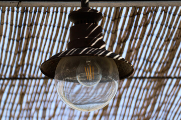 Large light bulb are golden brass lampshade with thatched roof in beach hut