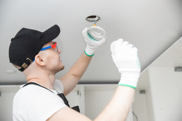 Working electrician changes light bulb and installs wiring for lamp in ceiling