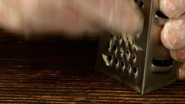 Chef hands rubbing clove of garlic on small metal grater on kitchen board. Close-up.