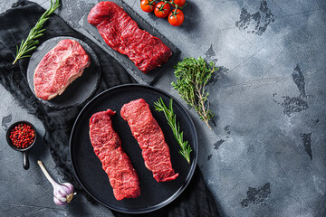 Raw denver, top blade,  tri tip steak on a black plate and stone slate with seasonings, herbs  grey...
