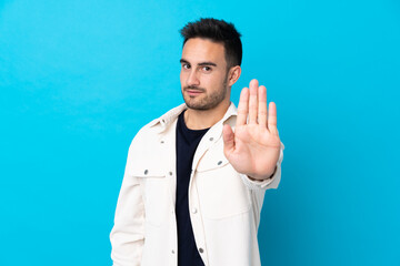 Young handsome man over isolated blue background making stop gesture with her hand