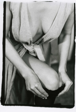 A young slender girl in clothes with a deep neckline puts on a stocking on her leg.