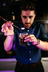 Professional bartender pouring and preparing rum and cola with lime at bar counter. Details of mixology