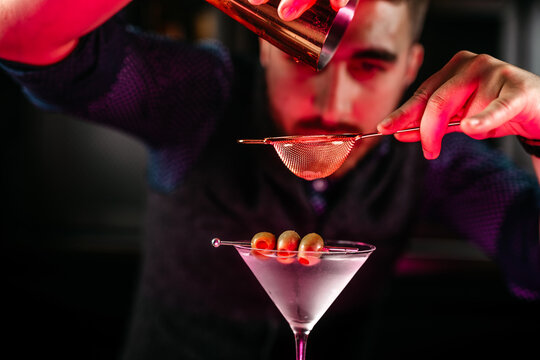 Professional Bartender Pouring And Preparing Martini With Olives At Bar Counter. Details Of Mixology