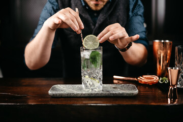 Professional bartender pouring and preparing gin and tonic with lime at bar counter. Details of...