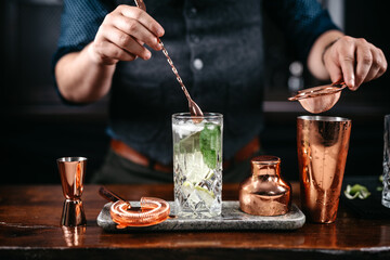 Professional bartender pouring and preparing mojito with lime at bar counter. Details of mixology