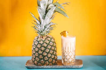details of pina colada alcoholic cocktail with rum, pineapple and ice on yellow and blue background