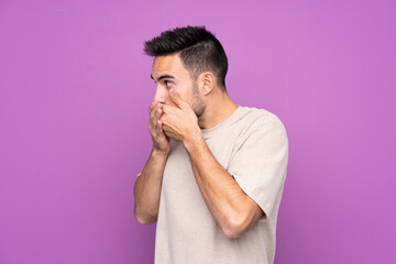 Young handsome man over isolated purple background covering mouth and looking to the side