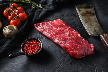 Raw, flap or flank, also known Bavette steak near butcher knife with pink pepper and rosemary. Black stone background. Side view vertical - obrazy, fototapety, plakaty