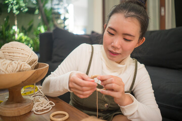 Asian girl enjoying macrame handcraft hobby - young happy and pretty Chinese woman at home doing macramé using ropes and cords and in domestic handmade decoration